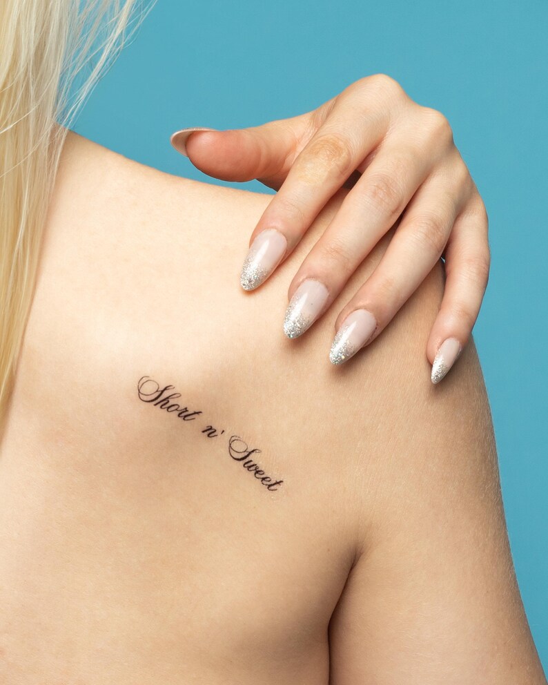 May include: A close-up of a person's shoulder with a small tattoo that reads "Short n' Sweet".
