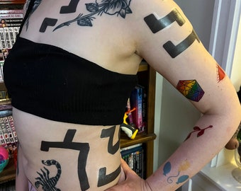 Puede incluir: Una persona con múltiples tatuajes de tinta negra en el pecho, los brazos y el torso. Los tatuajes incluyen una rosa, un engranaje, un escorpión y formas geométricas.