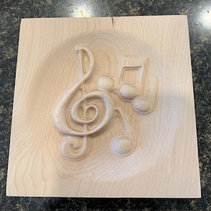 May include: A wooden plaque with a carved design of a treble clef and musical notes. The plaque is light brown and has a smooth surface.