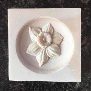 May include: A white ceramic cookie cutter in the shape of a daffodil flower.