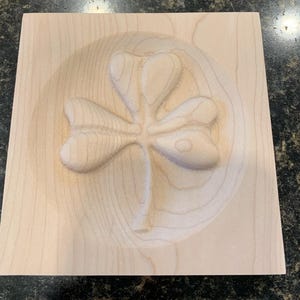 May include: A wooden plaque with a carved shamrock design. The shamrock is raised and has a detailed texture.