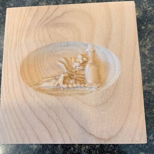 May include: A wooden block with a carved oval design featuring a detailed image of a pineapple with leaves.