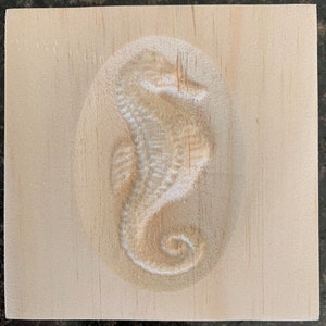 May include: A wooden block with a carved seahorse design. The seahorse is facing to the right and has a curled tail.