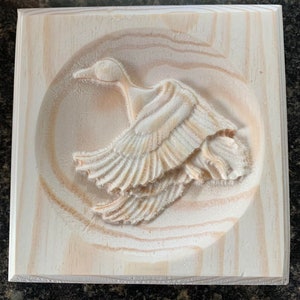 May include: A wooden wall plaque with a carved image of a bird in flight. The bird is carved in detail with its wings spread out.