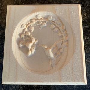 May include: A wooden square plaque with a carved design of a bird in a circle surrounded by flowers.