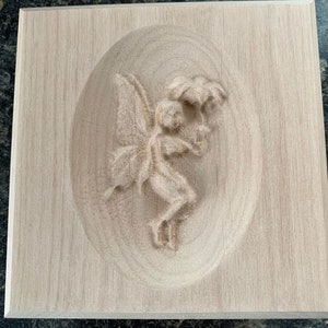 May include: A wooden plaque with a carved fairy design. The fairy is holding a flower and has wings. The plaque is a light brown color.