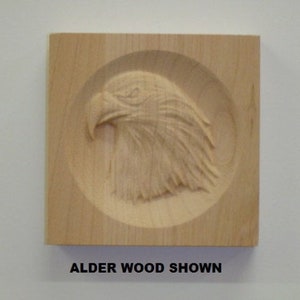 May include: A wooden plaque with a carved image of an eagle's head. The plaque is made of alder wood and has a natural finish. "ALDER WOOD SHOWN" is printed below the image.