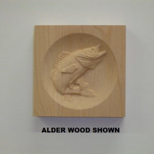 May include: A wooden plaque with a carved image of a fish jumping out of the water. The plaque is made of alder wood and has a natural finish. "Alder Wood Shown" is written below the image.