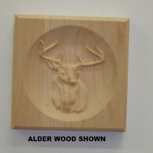 May include: A wooden plaque with a carved deer head in a circular frame. The plaque is made of alder wood and has a natural finish. "Alder Wood Shown" is printed below the plaque.
