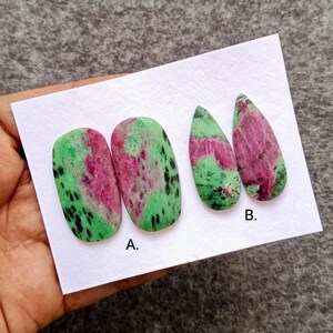 May include: Four polished ruby zoisite gemstones. Two are oval-shaped, labeled "A", and two are teardrop-shaped, labeled "B". The stones feature a mix of green, pink, and black colors.