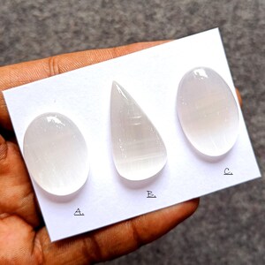 Puede incluir: Tres piedras de selenita pulidas de diferentes formas: ovalada, en forma de lágrima y otra ovalada. Las piedras son de color blanco translúcido y están dispuestas sobre una tarjeta blanca. Las letras A, B y C están escritas en la tarjeta.