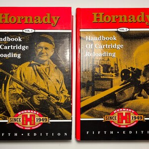 May include: Two hardcover books titled Hornady Handbook Of Cartridge Reloading, Vol. 1 and Vol. 2, Fifth Edition. The covers feature red and black designs with yellow-toned illustrations of individuals with rifles and the Hornady Since 1949 logo.