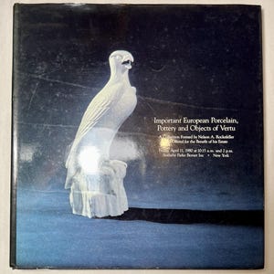 May include: A white porcelain eagle sculpture on a textured base, set against a dark blue background. The image is from a Sotheby's auction catalog, with text that reads "Important European Porcelain, Pottery and Objects of Vertu."