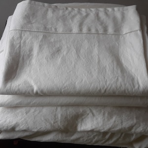May include: A stack of four white cotton pillowcases. The pillowcases are folded and stacked on top of each other.