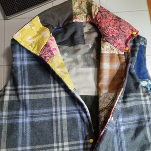 Könnte beinhalten: Eine graue karierte Weste mit einem Patchwork-Kragen. Der Kragen besteht aus verschiedenen Stoffen, darunter Blumenmuster, Karo und einfarbige Stoffe. Die Weste hat einen Reißverschluss und zwei Taschen.