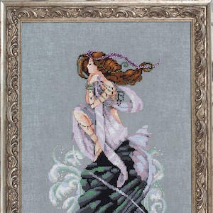 Puede incluir: Un bordado de punto de cruz que representa a una mujer con el pelo largo y castaño, vestida con un vestido morado fluido y de pie sobre un afloramiento rocoso con olas rompiendo a su alrededor.