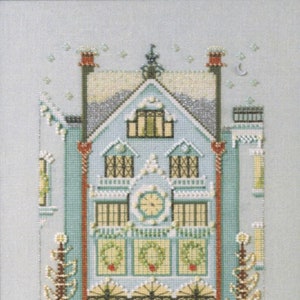 Peut inclure: Un motif de point de croix représentant une maison bleue avec des bordures blanches et une horloge sur la façade. La maison est décorée de couronnes et de lumières. Il y a deux arbres de chaque côté de la maison.