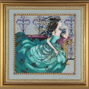 May include: A framed cross-stitch embroidery depicting a woman in a teal gown with gold accents, sitting on a purple and gold couch. The woman has long dark hair and is looking to the side. The background is a light blue with a floral pattern.