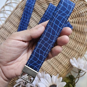 May include: A blue and white patterned fabric keychain with a silver key ring. The fabric has a geometric design with thin white lines on a dark blue background.