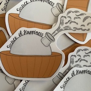 May include: A collection of stickers featuring a cartoon illustration. The design includes a brown bowl with a gray object inside, and a spout emitting a cloud-like shape. The text "Source of Happiness" is written in a script font.