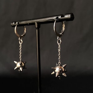 Op de afbeelding: Een paar zilveren oorbellen met een ketting en een hangende spijkerbal.