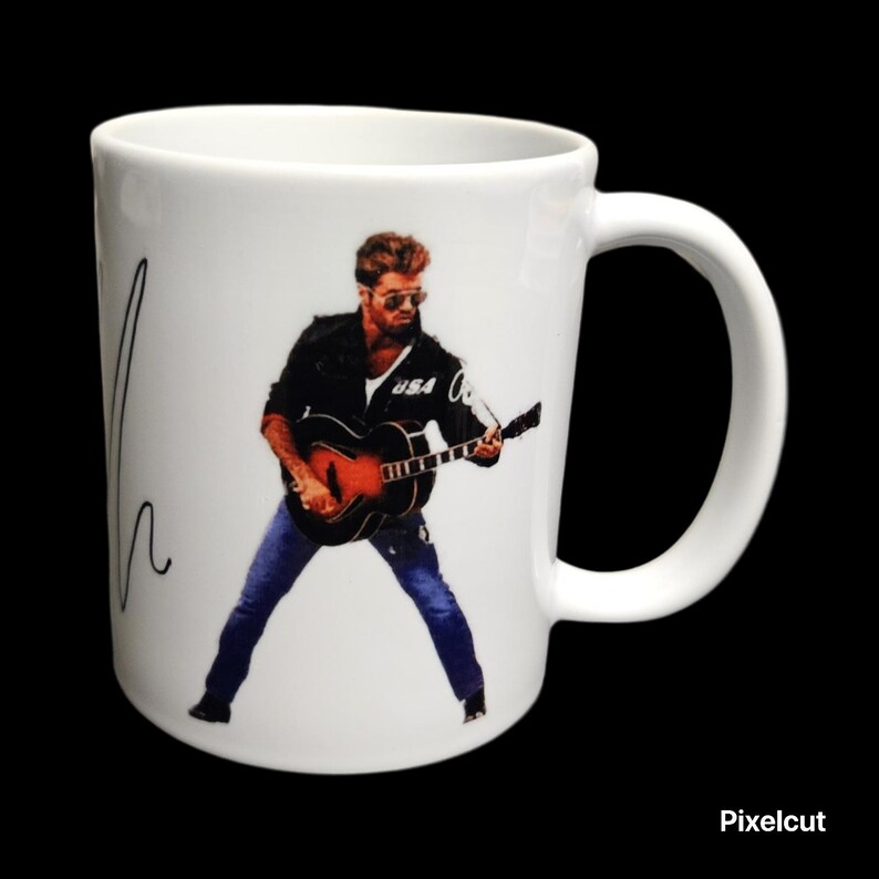 May include: White ceramic mug featuring a musician playing a guitar. The image shows the musician wearing sunglasses, a black jacket, and blue jeans. The mug has a curved handle and a signature on the side.