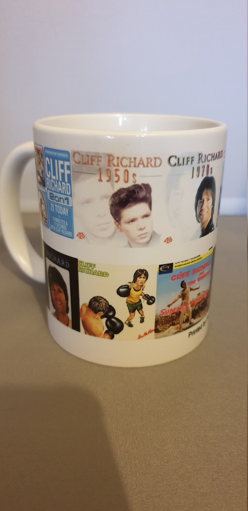 May include: White ceramic mug with a collage of Cliff Richard album covers from the 1950s and 1970s. The mug features images of Cliff Richard, album titles, and release dates.
