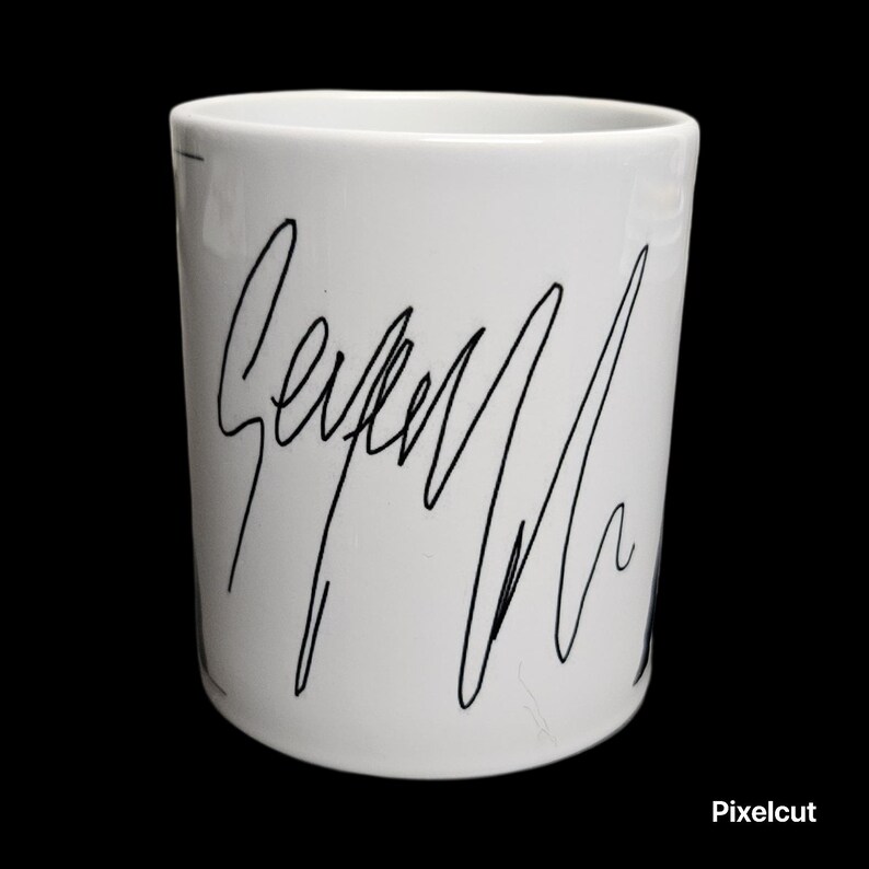 May include: White ceramic mug with a black handwritten signature design. The mug has a cylindrical shape and a smooth, glossy finish. The black signature is the primary design element, adding a unique touch to the mug.