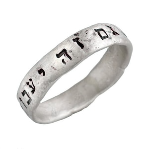 May include: A silver ring with Hebrew text inscribed on the band. The ring is worn and has a rustic finish.