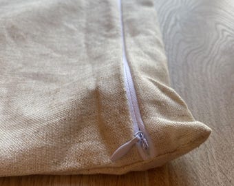 May include: A close-up of a beige pillow with a white zipper. The zipper is open and the pillow is lying on a wooden surface.