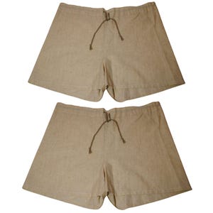 May include: Two pairs of beige linen shorts. Each pair features a drawstring waist and a relaxed fit. The shorts are made of a textured fabric, appearing lightweight and comfortable.
