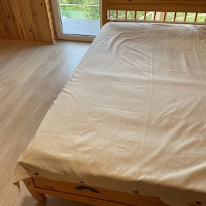 Op de afbeelding: Een beige bedsprei met een gladde textuur, die een houten bedframe met een lattenbodem bedekt.