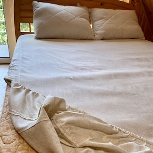 May include: A white fitted sheet with a beige fitted sheet tucked in around the edges. The fitted sheet is made of a linen material.