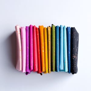 May include: A stack of colorful fabric squares in a rainbow of hues, from light pink to black. Each fabric piece is speckled with gold flecks. The fabrics are neatly folded and arranged, showcasing a spectrum of colors.