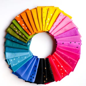May include: A circular arrangement of folded fabric in a rainbow of colors. Each fabric piece is a different color, ranging from red to purple to blue to green to yellow to orange. Some fabrics have a star pattern.