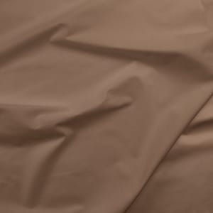 May include: A close-up shot of a tan fabric with visible folds and creases. The material has a smooth texture and a matte finish, with shadows creating depth and dimension. The fabric appears to be a solid color, suitable for various sewing and crafting projects.