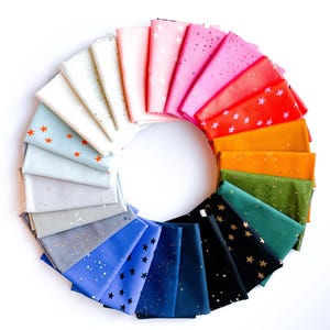 May include: A circular arrangement of folded fabric swatches in a spectrum of colors including white, pink, red, orange, green, blue, and black. Each piece of fabric features a repeating pattern of small stars or speckles in contrasting colors.