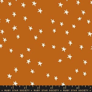 May include: A fabric with a repeating pattern of white stars scattered across a warm, orange-brown background. The stars are hand-drawn in a simple, whimsical style. The fabric is from Ruby Star Society.