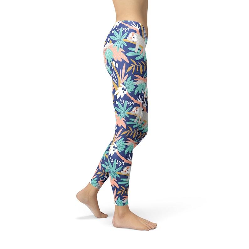 May include: Navy blue leggings featuring a repeating pattern of sloths, palm leaves, and tropical flowers in white, teal, coral, and yellow. The leggings are form-fitting and made of a stretchy material.