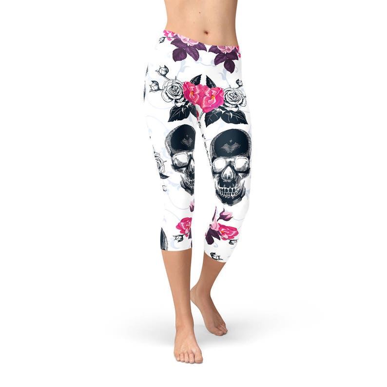 May include: White capri leggings with a repeating pattern of black skulls and pink roses. The leggings have a high waist and are made of a stretchy material. The floral and skull design creates a unique and edgy look.