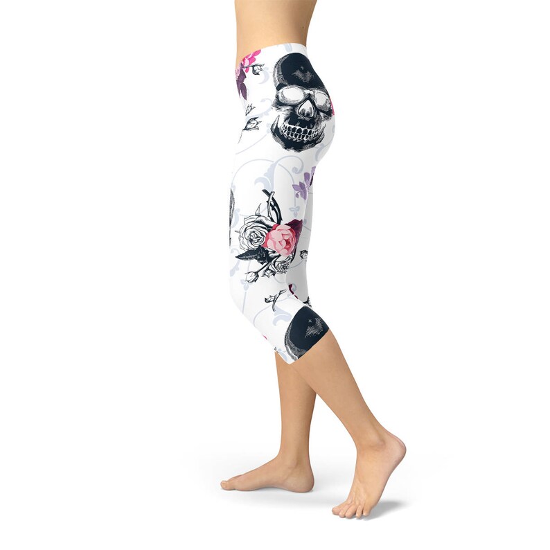 May include: White capri leggings with a repeating pattern of black skulls, pink roses, and purple butterflies. The leggings have a high waist and a cropped length, suitable for various activities.
