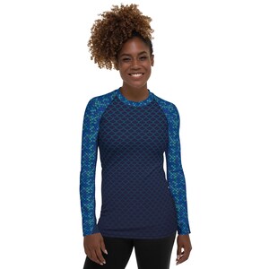 May include: A long-sleeved rash guard shirt with a mermaid scale pattern in shades of blue and teal. The shirt has a crew neck and is form-fitting. The sleeves and shoulders feature a lighter, more detailed scale design.