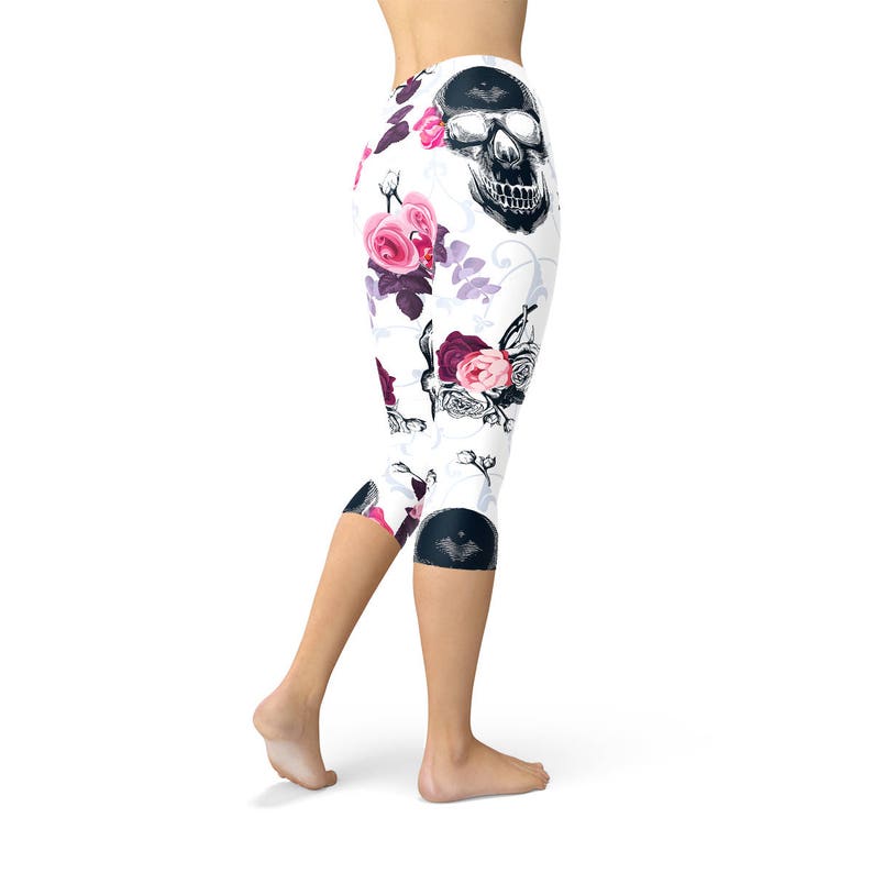 May include: White capri leggings with a repeating pattern of black skulls and pink and burgundy roses. The leggings have a high waist and end just below the knees. The floral and skull design creates a unique, edgy look.