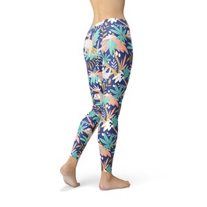 May include: Navy blue leggings with a colourful tropical pattern. The design features sloths, palm trees, and other foliage in shades of white, teal, coral, and yellow. The leggings are form-fitting and made of a stretchy material.
