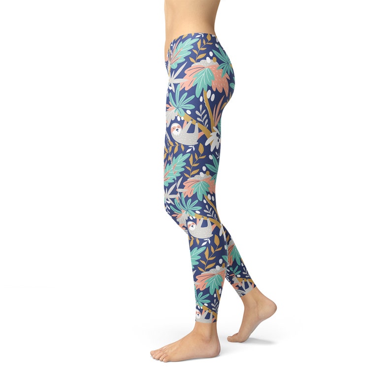 May include: Navy leggings featuring a repeating pattern of sloths, leaves, and flowers in grey, pink, and teal. The leggings are form-fitting and made of a soft, stretchy material.