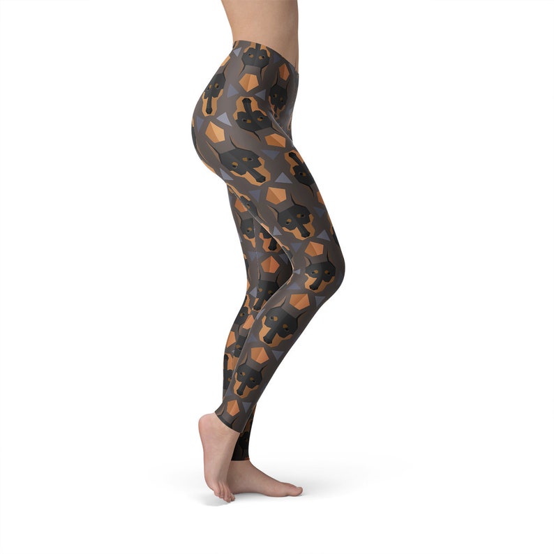 May include: Black leggings with a repeating pattern of brown and black Doberman Pinscher dog faces on a gray background.