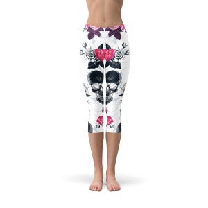 May include: White capri leggings with a repeating pattern of black skulls, pink and red roses, and floral accents. The leggings have a high waist and are made of a stretchy material.
