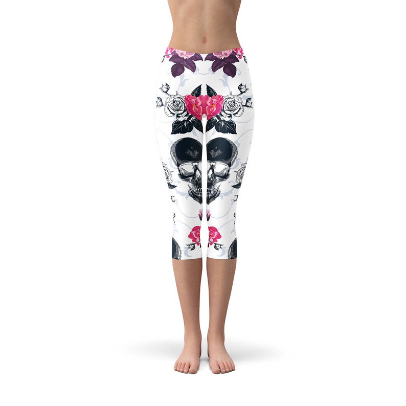 May include: White capri leggings with a repeating pattern of black skulls, pink and red roses, and floral accents. The leggings have a high waist and are made of a stretchy material.