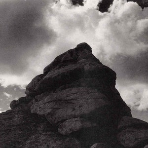 May include: A black and white photograph of a large rock formation with a cloudy sky in the background.