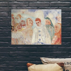 May include: A framed print of a painting depicting a group of figures in a theatrical setting. The artwork features a central figure in a white costume with blue buttons, surrounded by other characters with expressive faces and costumes. The color palette includes muted tones of beige, blue, and red.